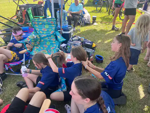 Shredders girls in NJ GRiT jerseys braid each other's hair at the team tent between races.