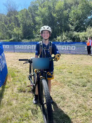 A smiling Shredders rider stands with his mountain bike after a race.