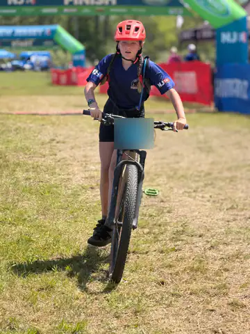 A Shredders rider in a red helmet walks her bike in after finishing a race.
