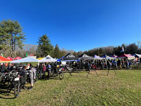 The busy race-day pit area with team tents and bikes on a bright spring morning.