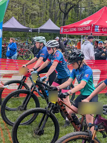 Girls line up on their mountain bikes at the start of a race, beside the NICA Girls Riding Together tent.