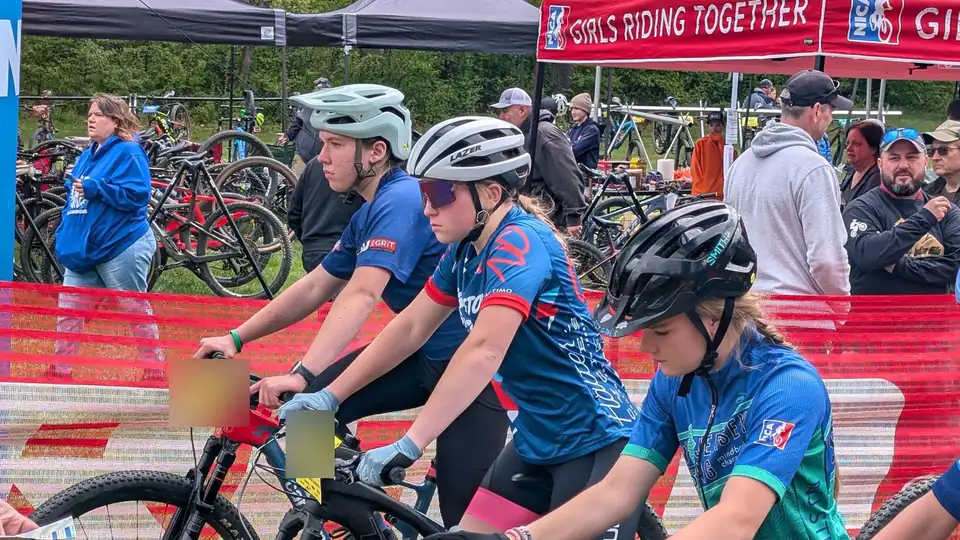 Girls line up on their mountain bikes at the start of a race, beside the NICA Girls Riding Together tent.