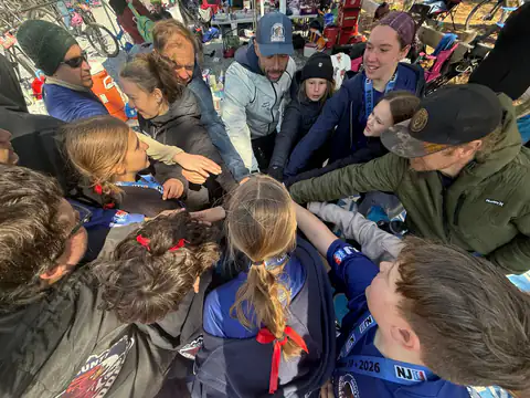 Shredders riders, coaches and parents stack hands in a team huddle before a race.