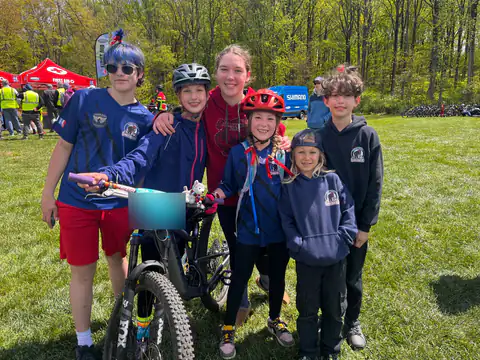 Six smiling Sussex County Shredders riders in team gear pose together with a mountain bike at a race.