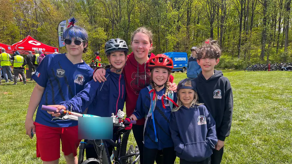 Six smiling Sussex County Shredders riders in team gear pose together with a mountain bike at a race.