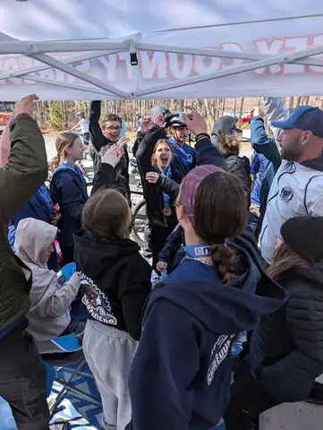Shredders riders and coaches cheer with raised arms under the team tent after a race.